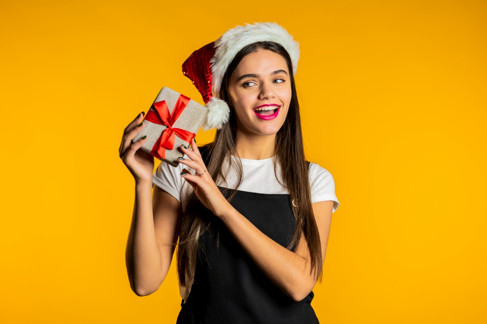 Young cute woman with present gift box on yellow studio background. Lady in Santa hat. New year mood. High quality photo. Young cute woman with present gift box on yellow studio background. Lady in Santa hat. Christmas, New year mood.