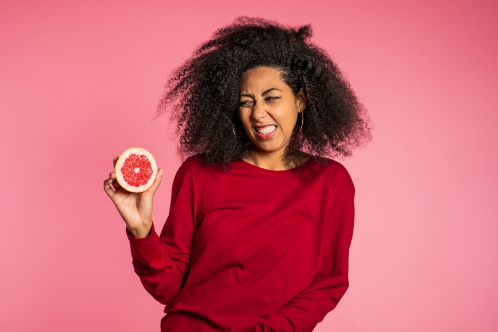 African american woman act ape her face from grapefruit cid. Lady grimaces. Curly hairstyle on pink background. Diet. healthy lifestyle concept. High quality photo. African american woman act ape her face from grapefruit cid. Lady grimaces. Curly hairstyle on pink background. Diet. healthy lifestyle concept
