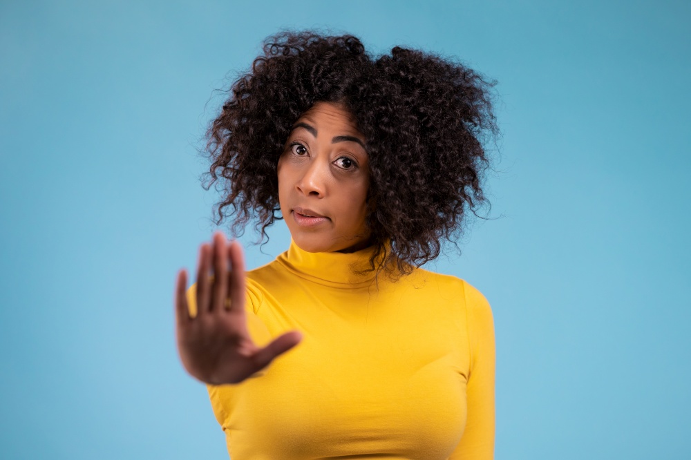 Mixed race woman disapproving with NO hand sign gesture. Denying, rejecting, disagree, portrait of beautiful girl on blue background.. Mixed race woman disapproving with NO hand sign gesture. Denying, rejecting, disagree, portrait of beautiful girl on blue background