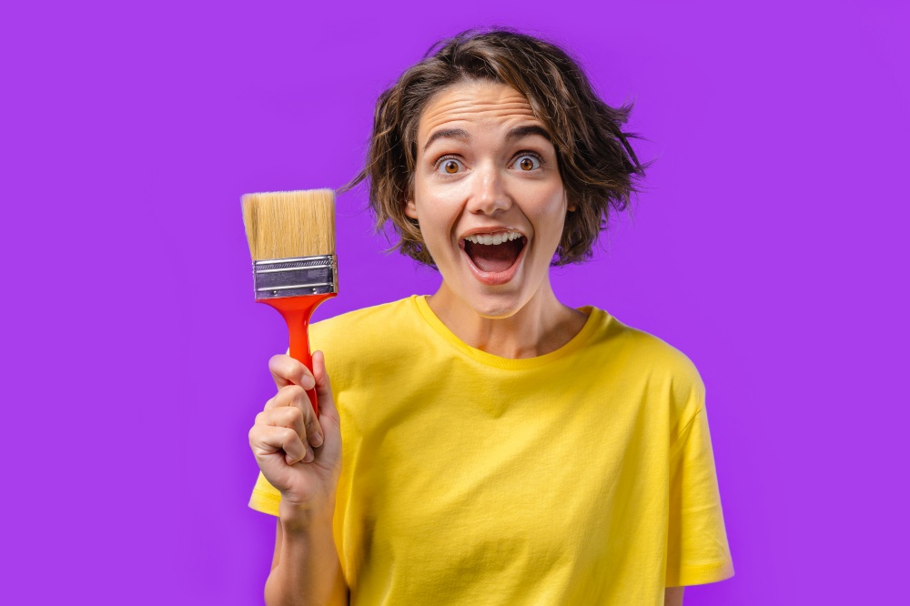 Happy woman artist with painting brush on violet background. Creative person, fantasy, idea, non-standard approach to life, repair in apartment. High quality photo. Happy woman artist with painting brush on violet background. Creative person, fantasy, idea, non-standard approach to life, repair in apartment