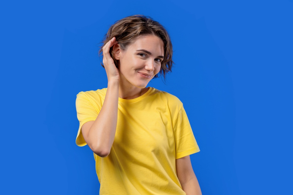 Playful woman smiling, flirting to camera on blue studio background. Cute cheerful lady in yellow t-shirt. High quality photo. Playful woman smiling, flirting to camera on blue studio background. Cute cheerful lady in yellow t-shirt.