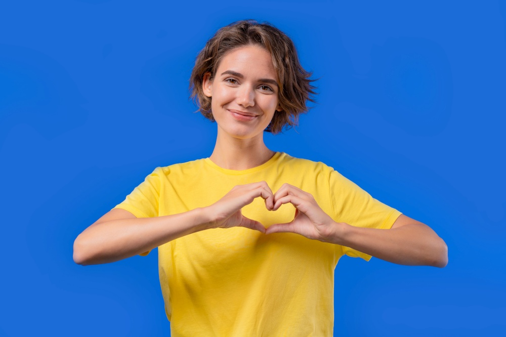 Smiling pretty woman showing sign of shape heart. Positive lady on blue background. Women health, volunteering, charity donation, gratitude symbol, flirting concept. High quality photo. Smiling pretty woman showing sign of shape heart. Positive lady on blue background. Women health, volunteering, charity donation, gratitude symbol, flirting concept.