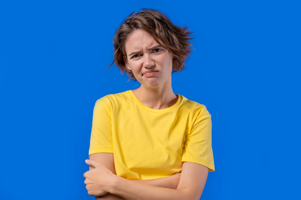Bored upset woman on blue background. Pretty lady in displeasure, she is tired of situation, empty promises, talks. High quality photo. Bored upset woman on blue background. Pretty lady in displeasure, she is tired of situation, empty promises, talks