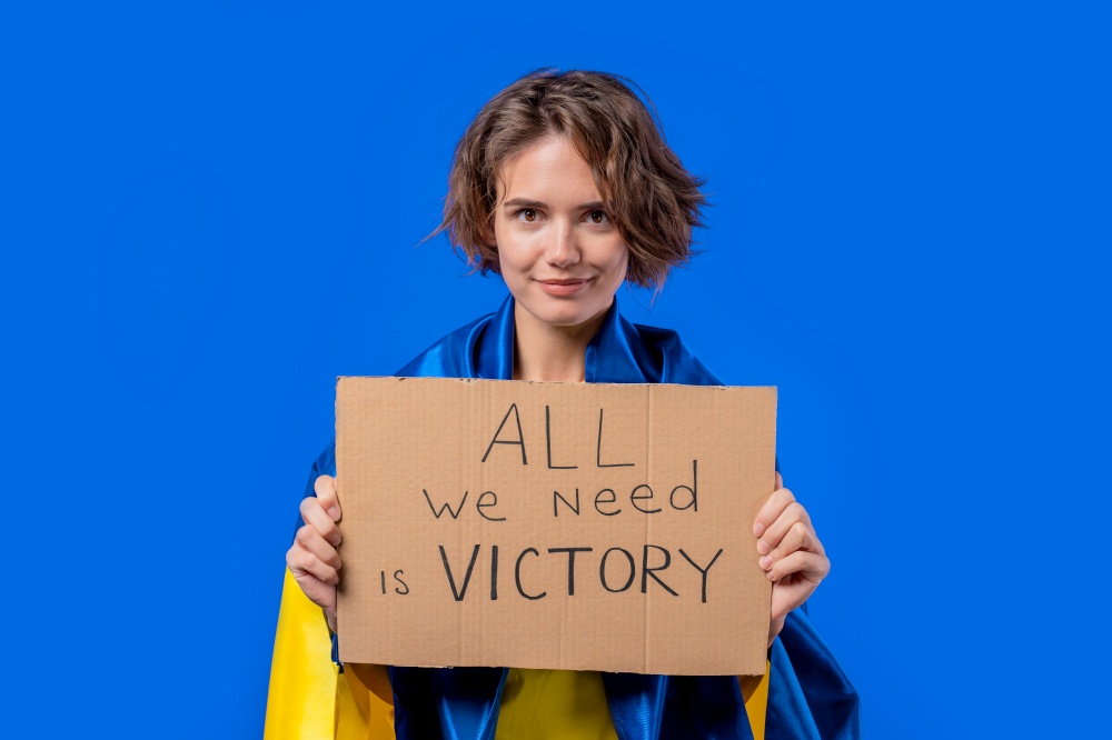 Ukrainian woman with cardboard All we need is victory on blue background. Ukraine will win war. Democracy, liberty, demonstration, russian aggresion concept. High quality photo. Ukrainian woman with cardboard All we need is victory on blue background. Ukraine will win war. Democracy, liberty, demonstration, russian aggresion concept