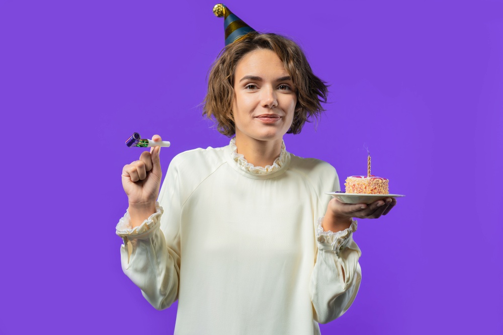 Happy birthday woman making wish - candle on cake. Girl smiling, celebrating anniversary. Young stylish lady on violet background. High quality photo. Happy birthday woman making wish - candle on cake. Girl smiling, celebrating anniversary. Young stylish lady on violet background.