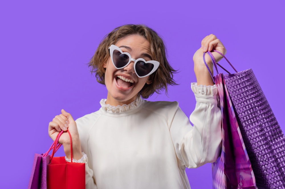Excited woman with colorful paper bags after shopping on violet studio background. Concept of seasonal sale, purchases, spending money on gifts. High quality photo. Excited woman with colorful paper bags after shopping on violet studio background. Concept of seasonal sale, purchases, spending money on gifts