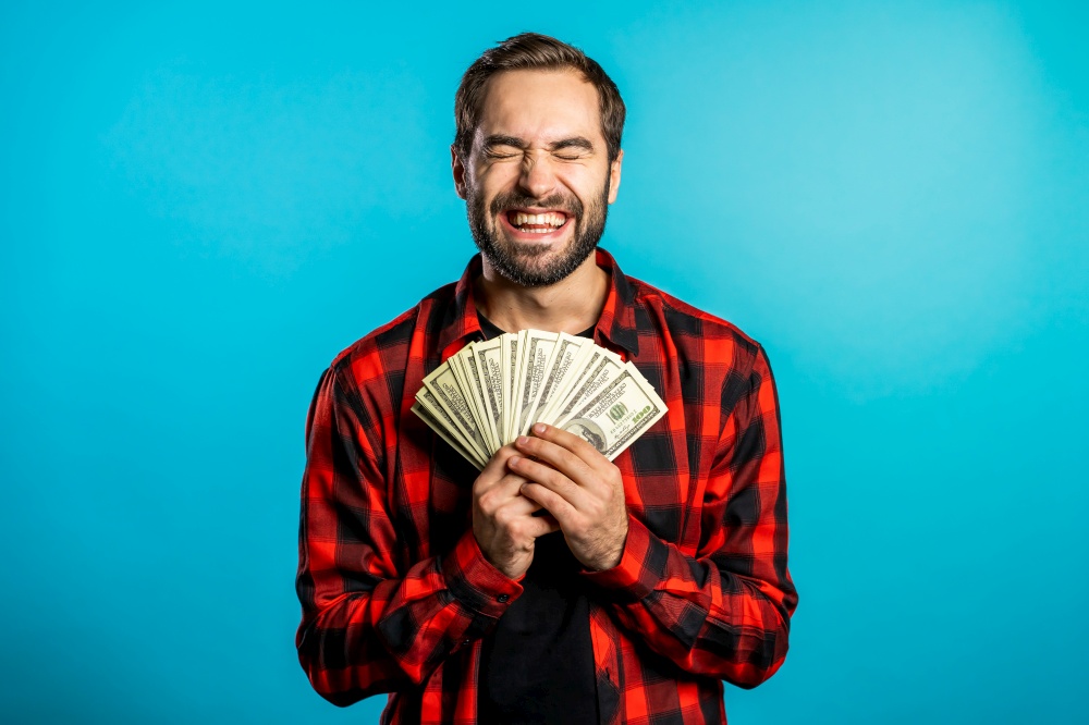 Satisfied happy excited man showing money - U.S. currency dollars banknotes on blue wall. Symbol of success, gain, victory. Satisfied happy excited man showing money - U.S. currency dollars banknotes on blue wall. Symbol of success, gain, victory.