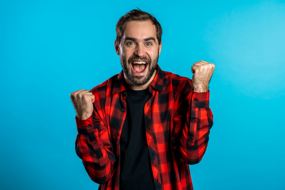 Yes winner gesture. Happy european man rejoices. Handsome guy with stylish beard surprised to camera over blue background. Yes winner gesture. Happy european man rejoices. Handsome guy with stylish beard
