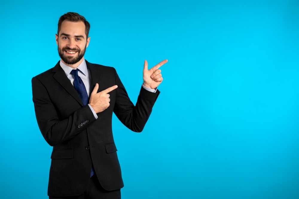 Happy smiling businessman in corporate suit presenting, showing something isolated on blue background. Portrait of man, he pointing with arms on his left with copy space. Happy smiling businessman in corporate suit presenting, showing something isolated on blue background. Portrait of man, he pointing with arms on his left with copy space.