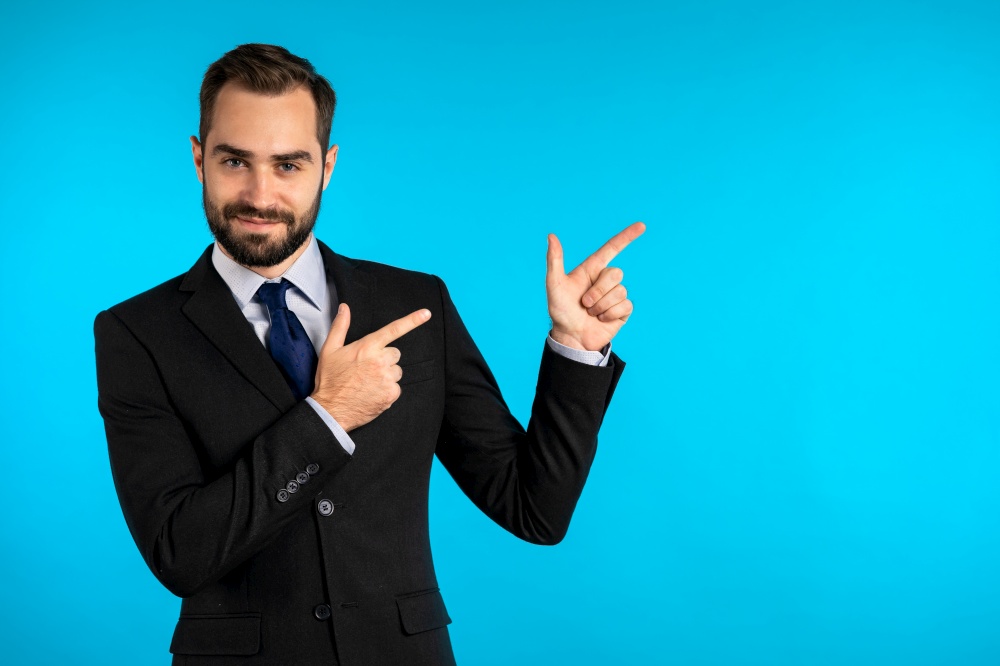 Happy smiling businessman in corporate suit presenting, showing something isolated on blue background. Portrait of man, he pointing with arms on his left with copy space. Happy smiling businessman in corporate suit presenting, showing something