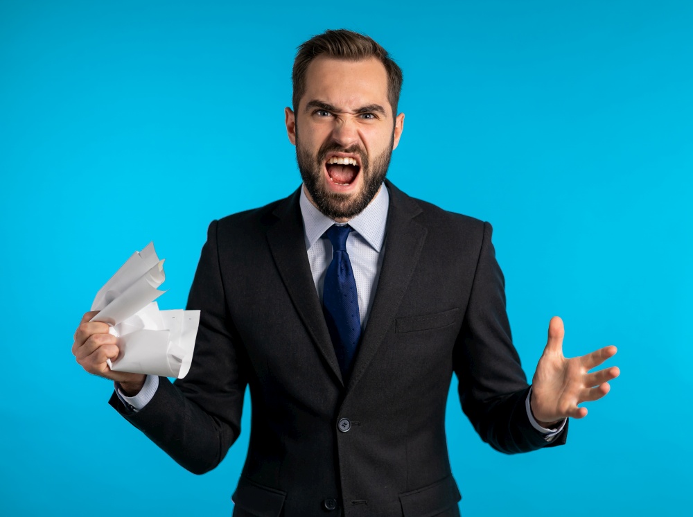 Serious businessman tearing contract in pieces. Angry furious male office worker throwing crumpled paper, having nervous breakdown at work, screaming in anger, stress management. Serious businessman tearing contract in pieces. Angry furious male office worker