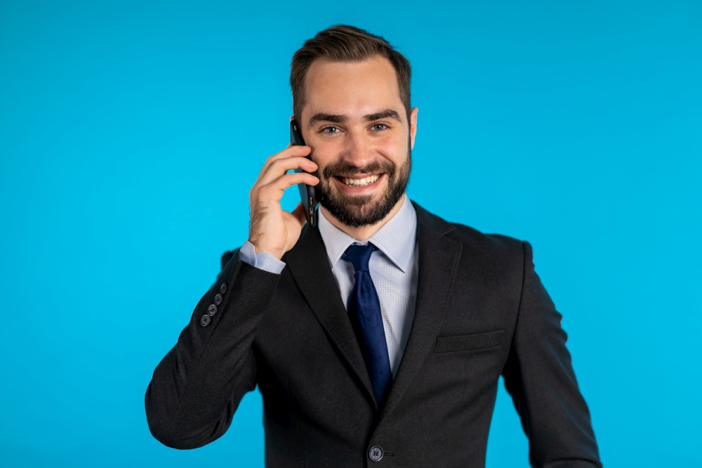 Businessman have conversation using mobile phone isolated on blue background. Business guy in formal suit gladly talks with colleague. Office employee, wage worker, weekdays concept.. Close up portrait of businessman have conversation using mobile phone.