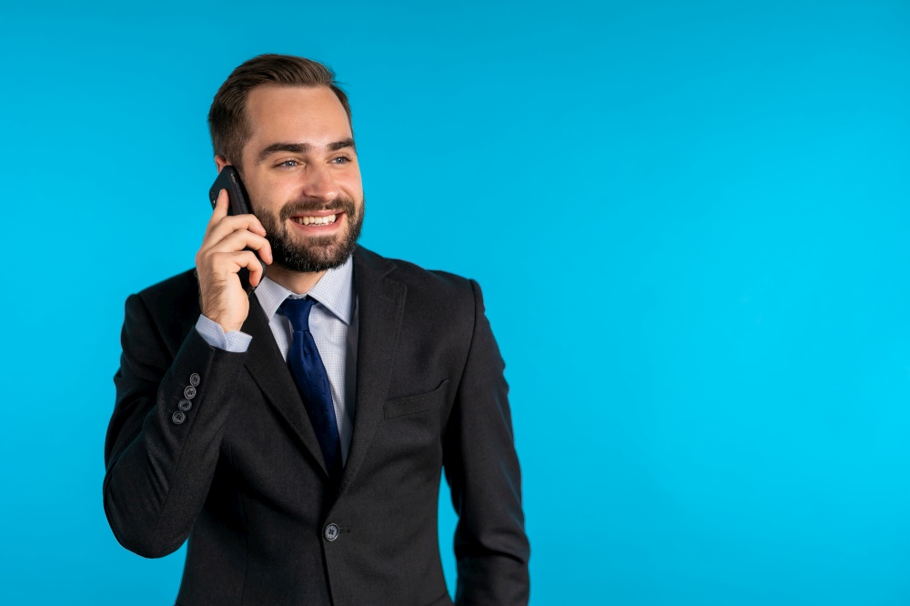 Businessman have conversation using mobile phone isolated on blue background. Business guy in formal suit gladly talks with colleague. Office employee, wage worker, weekdays concept.. Businessman have conversation using mobile phone isolated on blue