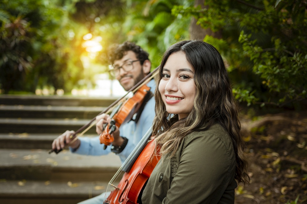 Portrait of two young violists sitting outside. Man and woman violinist sitting on the stairs. Two young violinists sitting outdoors looking at the camera. Concept of two young violinists