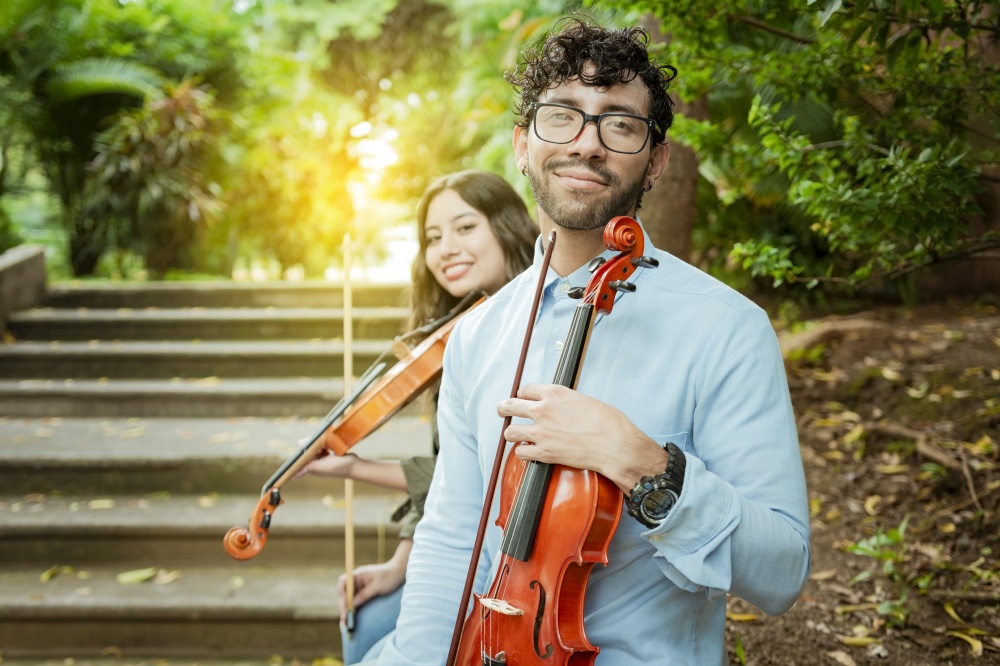Portrait of two young violists sitting outside. Man and woman violinist sitting on the stairs. Concept of two young violinists, Two young violinists sitting outdoors looking at the camera