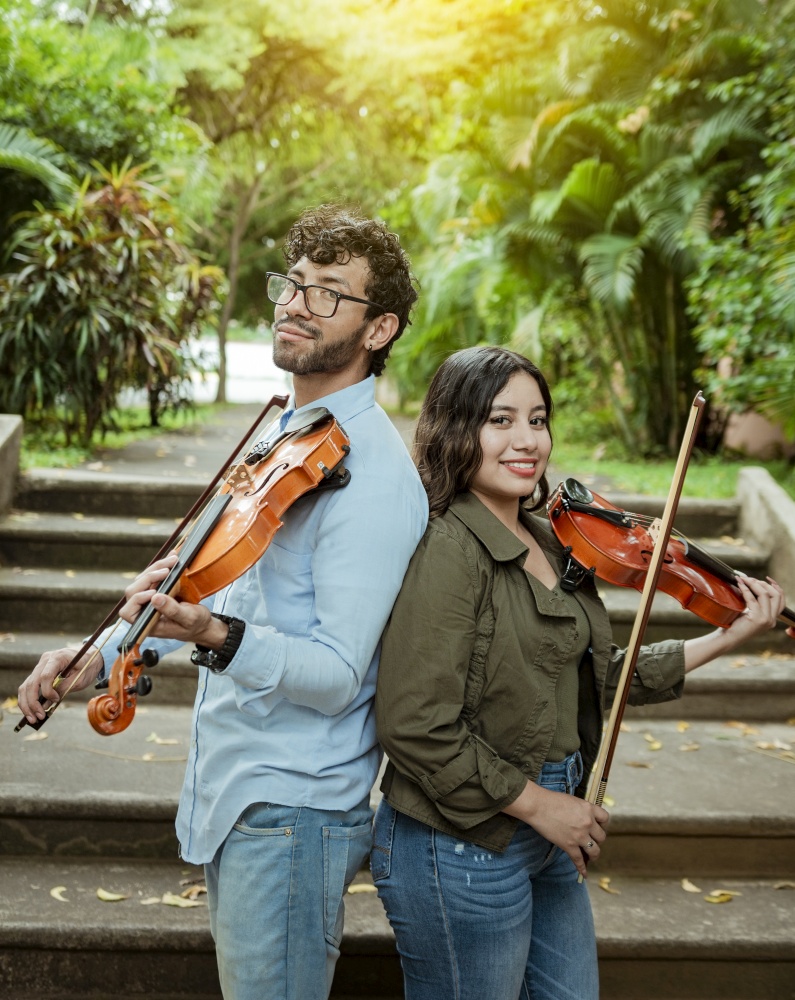 Portrait of two young violists back to back outdoors. Portrait of smiling male and female violinist back to back outdoors. Two young violinists back to back holding their violins
