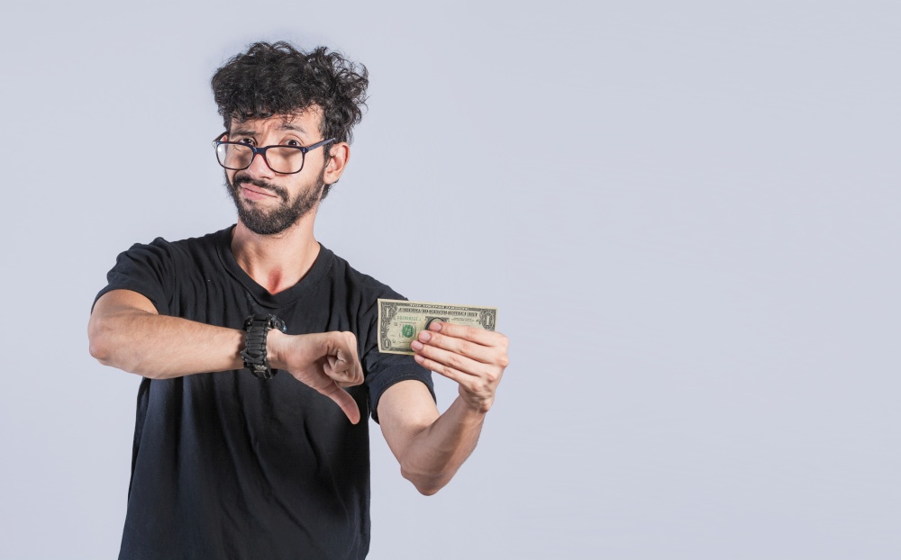Sad person holding a banknote with his thumb down, Sad man with a dollar bill, Concept of man with money problems