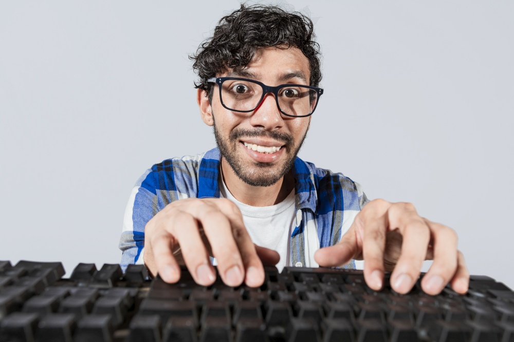 Portrait of nerdy man in front of keyboard, Cheerful nerdy guy with hands on keyboard. Funny nerdy person in front of the keyboard smiling at the camera