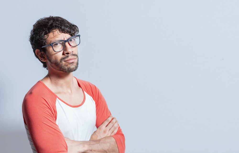 Young latin man in glasses with crossed arms looking in profile at the camera. Nicaraguan man with crossed arms looking at the camera isolated, Portrait of young man with crossed arms isolated