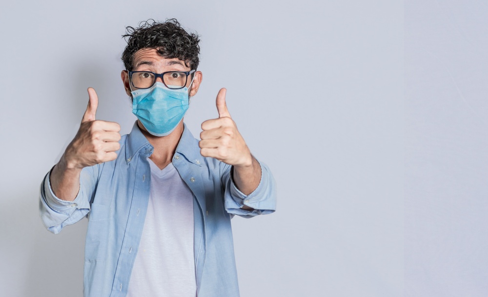 Man wearing medical mask and giving thumbs up, Isolated person wearing medical mask giving thumbs up.