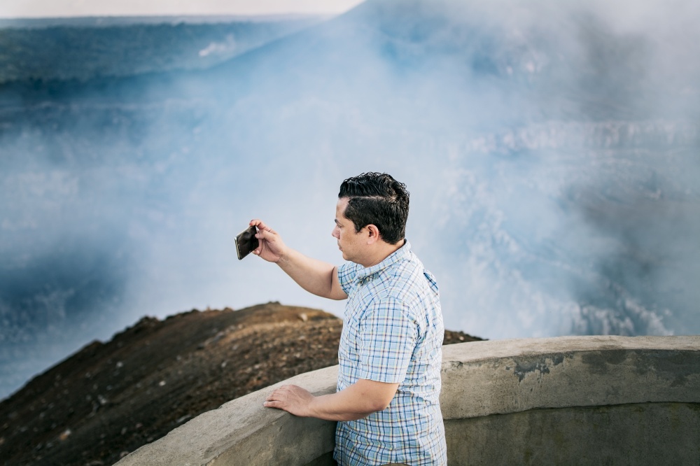 Tourist man taking photos at a viewpoint. Young tourist man taking photos at a volcanic viewpoint. Adventurous man with his cell phone taking photos at a viewpoint