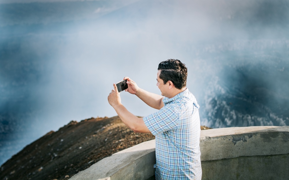 Young tourist man taking photos at a volcanic viewpoint. Adventurous man with his cell phone taking photos at a viewpoint, Tourist man taking photos at a viewpoint