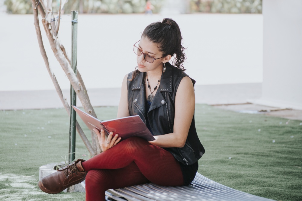A student girl reading a book, urban girl sitting on a bench reading a book, Latin girl reading a book outside