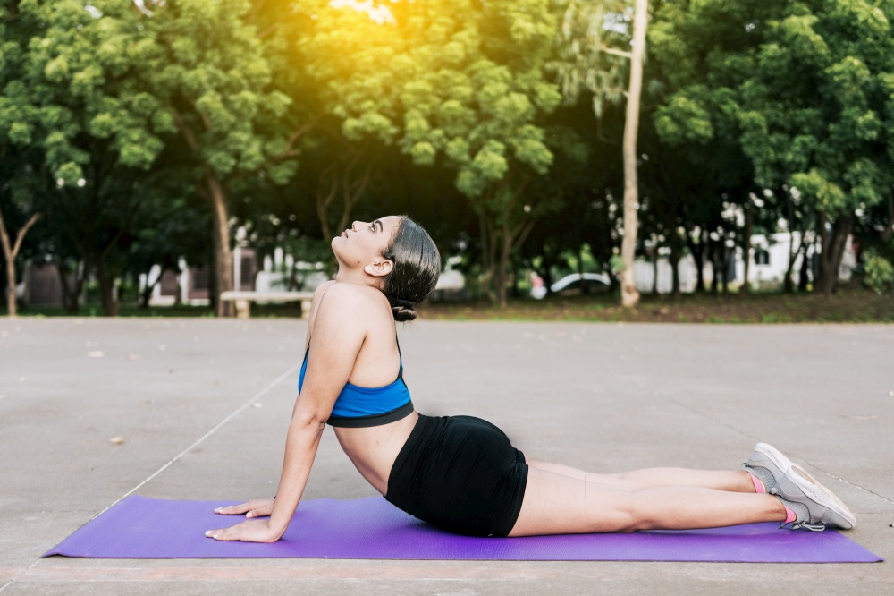 Sporty woman stretching her body doing cobra pose in a park. Athlete woman doing cobra pose in a park. Athlete woman doing yoga Bhujangasana in a park