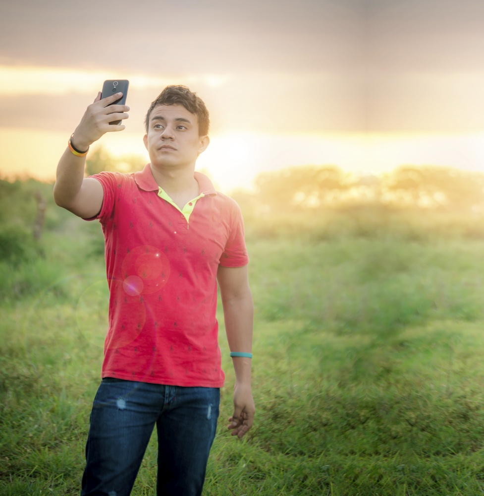 Young man taking a picture, young man taking selfie in the field, young man in the field taking a picture