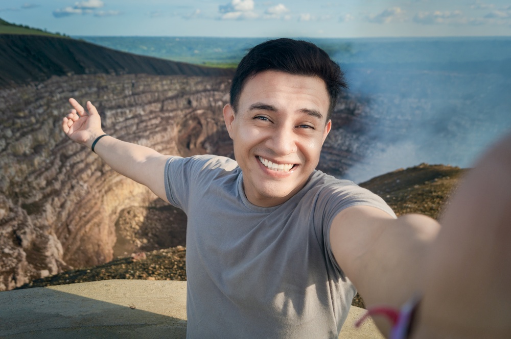 Tourist taking a selfie at a viewpoint. Handsome tourist taking a selfie on vacation. Adventurous man taking a selfie at a viewpoint. Close up of person taking an adventure selfie