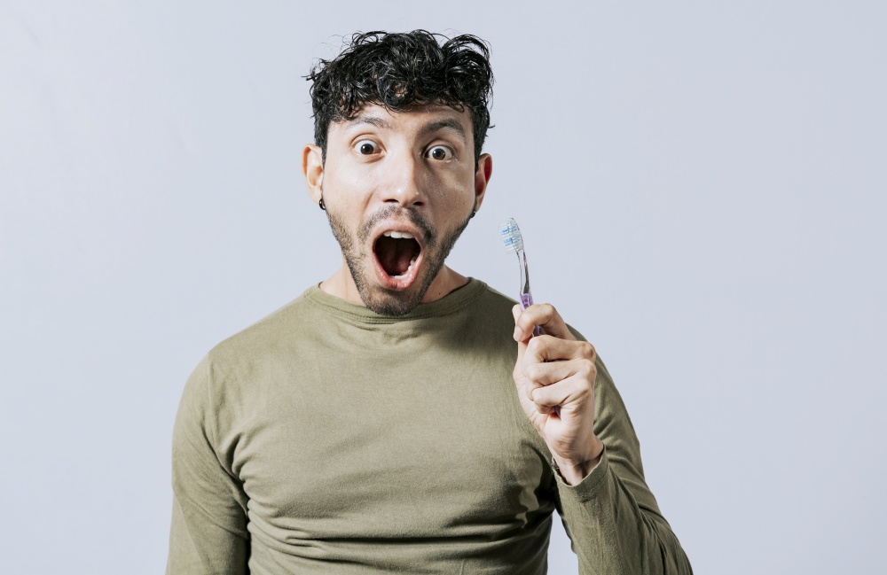 Surprised young man holding a toothbrush. Amazed teenager holding toothbrush isolated, Guy holding toothbrush with amazed face isolated on white