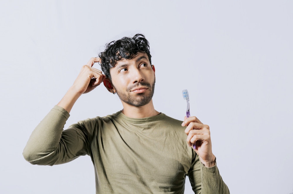 Thoughtful man holding toothbrush isolated, Portrait of young man thinking holding toothbrush. Man holding toothbrush with pensive expression isolated. Person holding toothbrush looking up