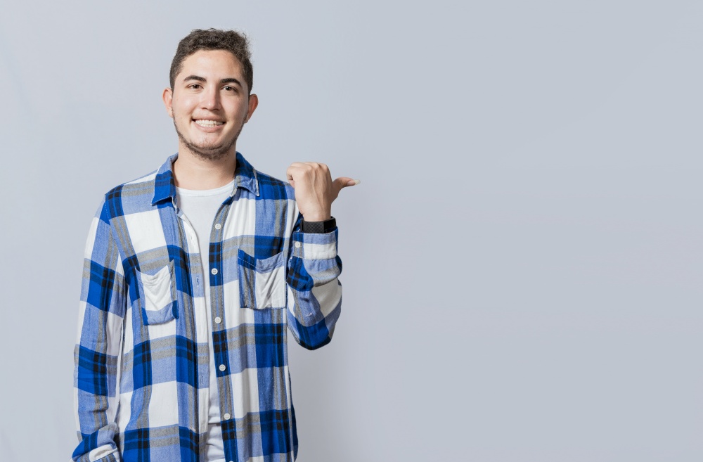 Cheerful guy with friendly smile pointing to the side isolated. Smiling young man pointing with one hand a promotion to the side. Concept of handsome man pointing an advertisement isolated