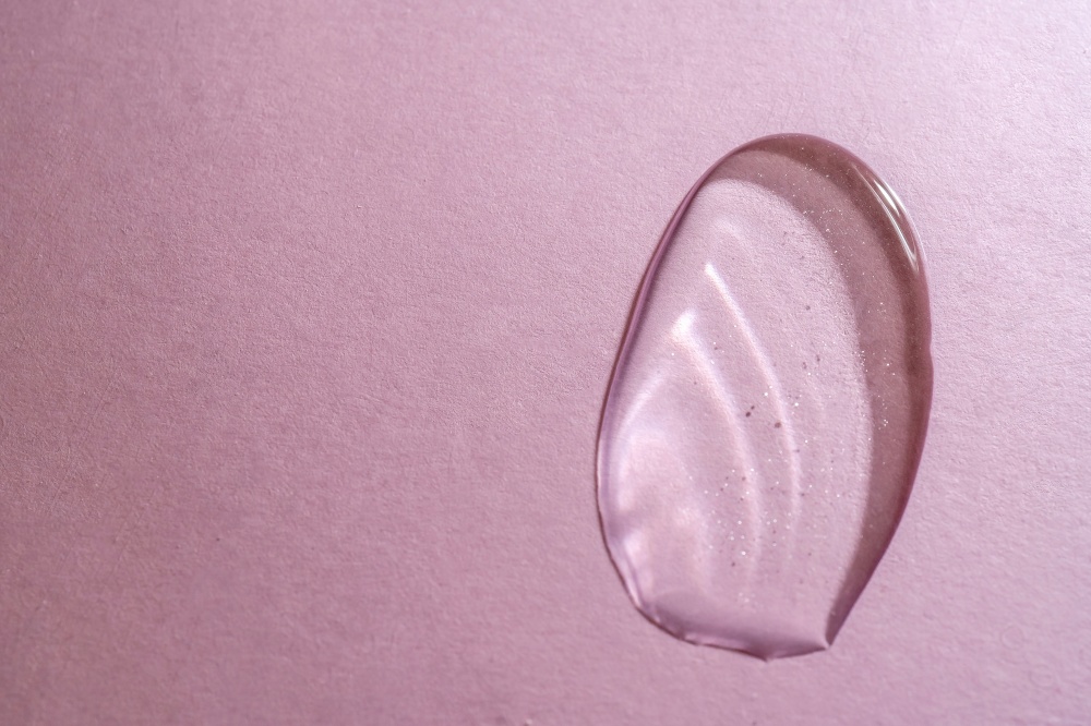 A drop of transparent cosmetic gel on a pink background. Perfect for demonstrating the consistency of your gel or serum.. A drop of transparent cosmetic gel on a pink background