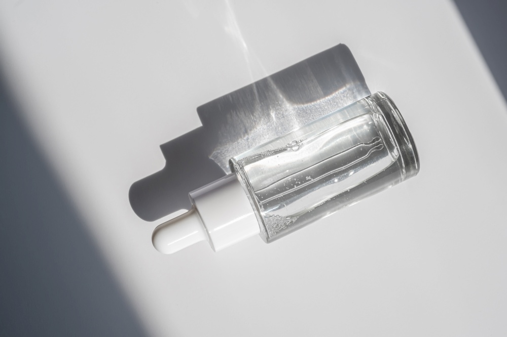 A white transparent bottle with serum in the rays of the sun. Laconic bottle shape.. A white transparent bottle with serum in the rays of the sun.