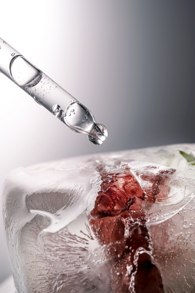 Pipette on a large piece of ice with frozen flowers. A wonderful concept for cosmetics and perfumes.. Pipette on a large piece of ice with frozen flowers.