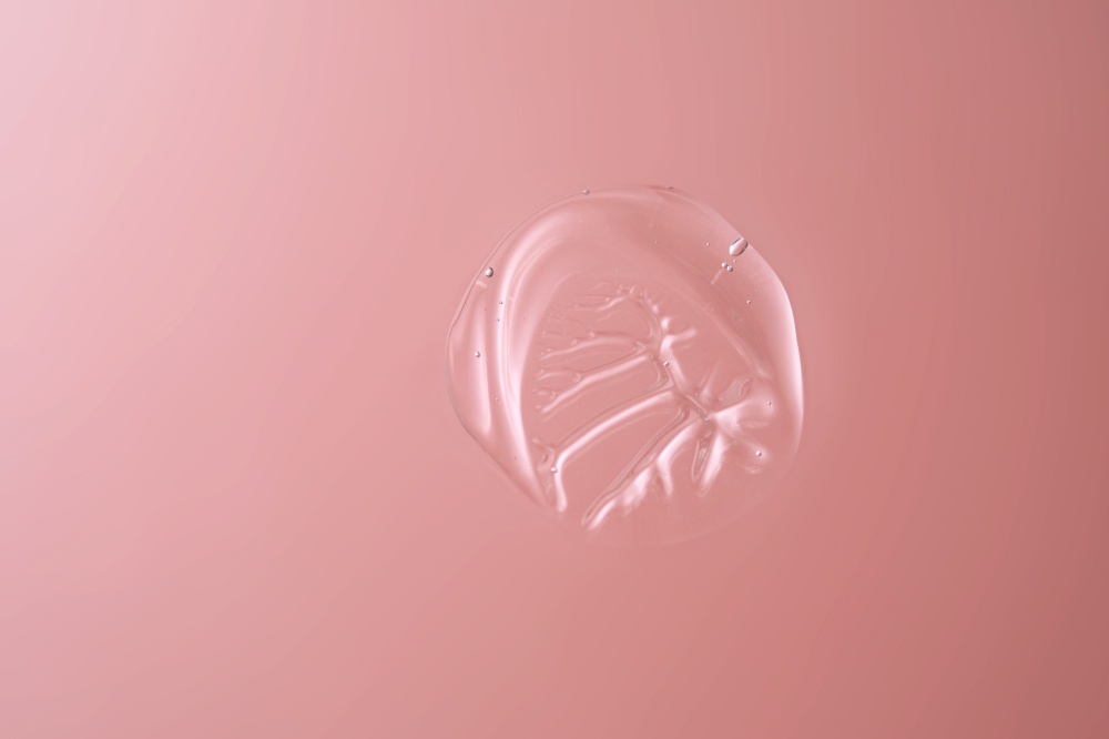 Drop of cosmetic transparent gel on a pink background. The texture of the serum, heir gel or hyaluronic booster.