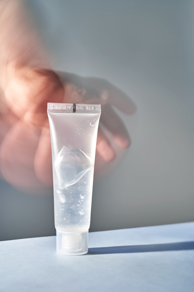 A transparent bottle of cosmetic gel with a blurred hand on the background. Suitable for advertising shower gel, shampoo and other care products.. A transparent bottle of cosmetic gel with a blurred hand on the background.