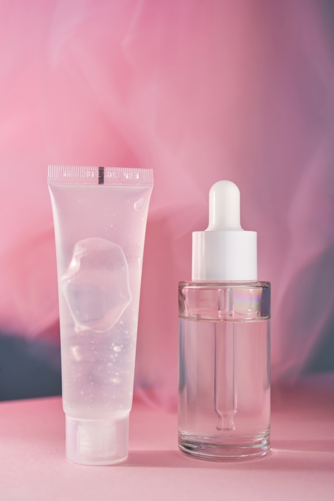 A transparent bottle of cosmetic gel and a bottle of serum on a pink background. Gentle photo of cosmetics.. A transparent bottle of cosmetic gel and a bottle of serum on a pink background.
