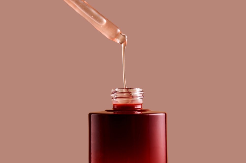 A drop of pink cosmetic drips from the dropper into a burgundy bottle.. A drop of pink cosmetic drips from the dropper.