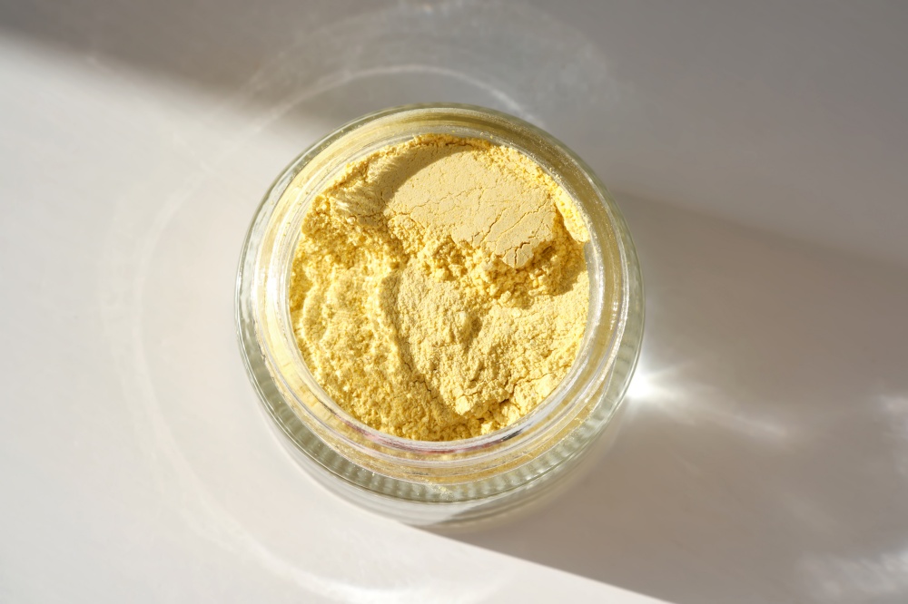 An open jar of a yellow turmeric facial enzime scrub showing off its texture.. An open jar of a yellow turmeric facial scrub showing off its texture.