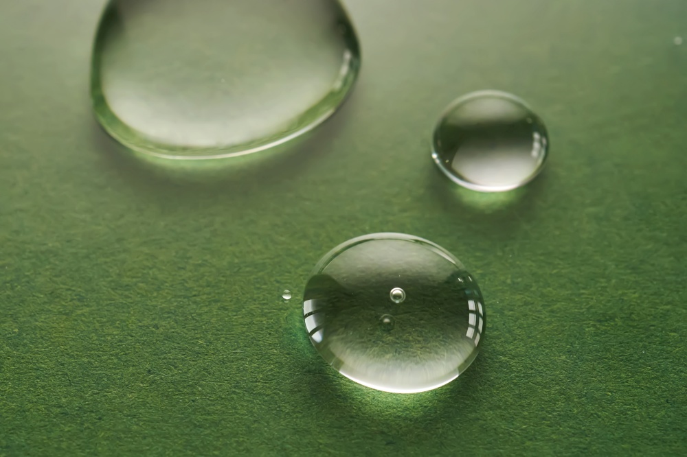 Three drops on a green background.. Three drops of liquid on a green background.