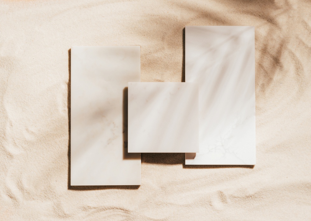 Creative summer podium of marble tiles on the background of sand. Top view, copy space, bright sunlight and shadows. Showcase template for trendy natural cosmetics product with place for text, mockup. Creative summer podium of marble tiles background of sand, copy space, sunlight and shadows, mockup