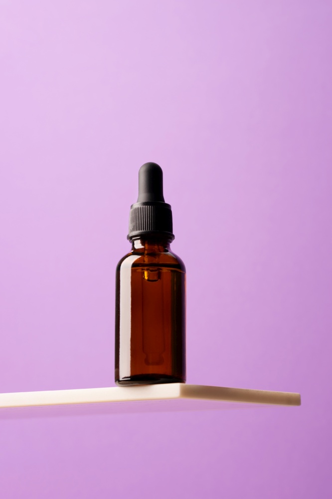 A bottle of a cosmetic product, made of dark glass with a pipette on a creative marble shelf, podium purple background. Angle below eye level, look up. Bottle of cosmetic product, dark glass with pipette creative marble shelf, podium purple background