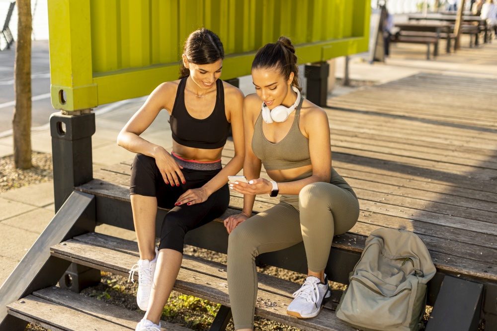 Pretty young women in sportswear looking at mobile phone after exercise training