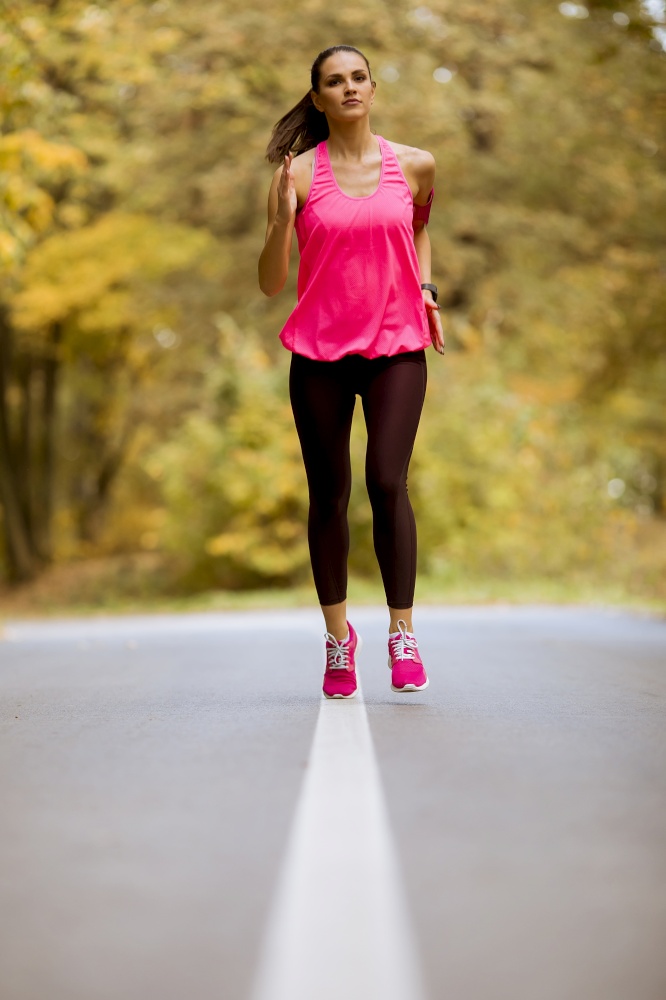 Young fitness woman running at  forest trail in autumn