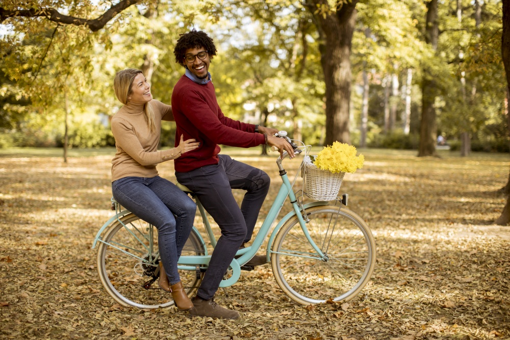 Multiracial young couple riding on a bicycle at the autumn park