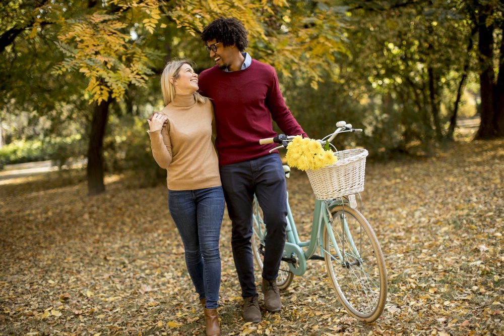 Multiracial young couple with bicycle walking in the autumn park
