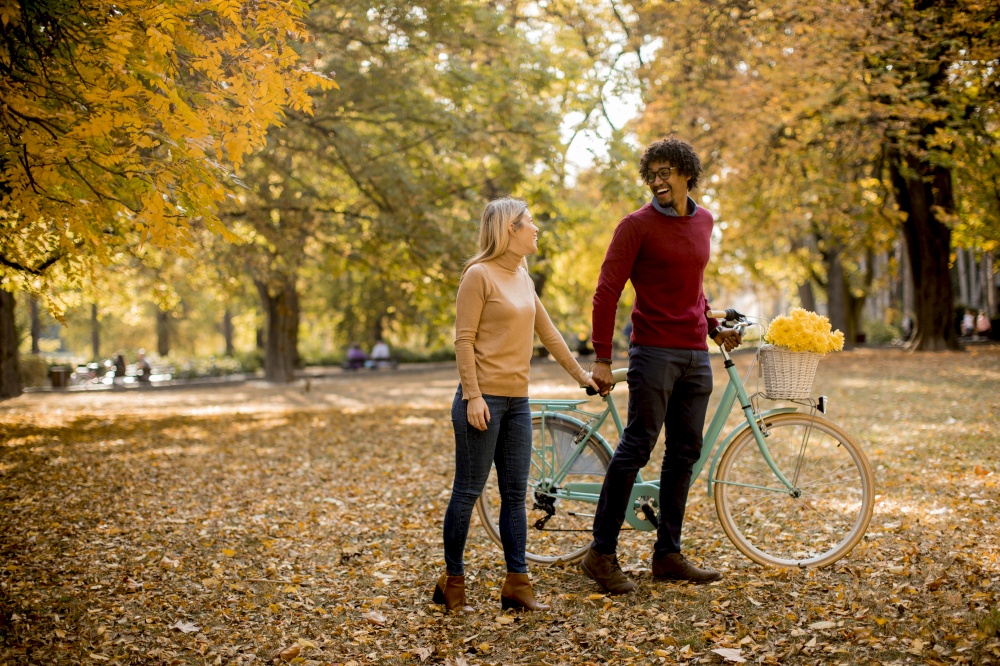 Multiracial young couple with bicycle standing in the autumn park