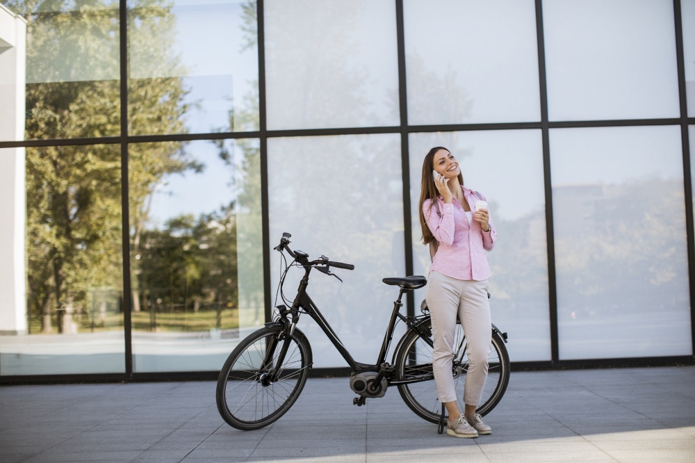 Pretty young woman using mobile phone by modern city electric e-bike as clean sustainable urban transportation